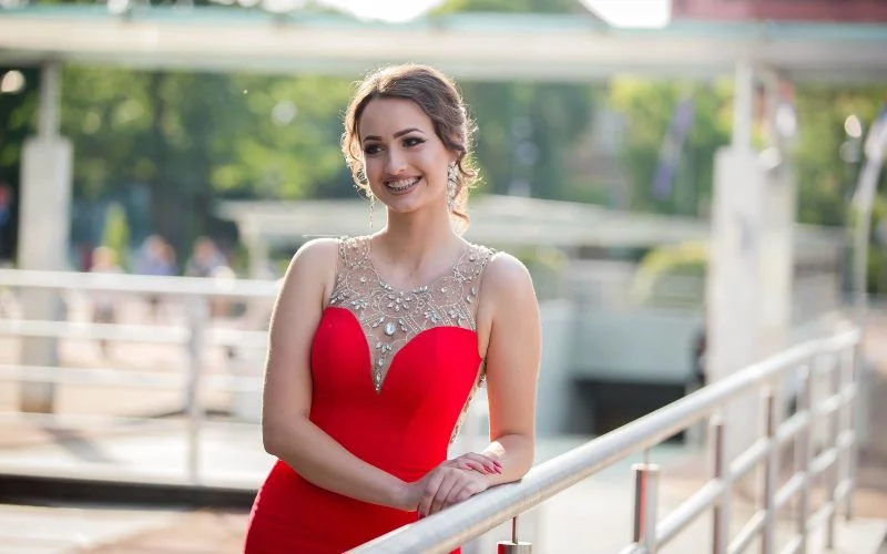 Prom picture pose for girls with a woman in a red gown posing by a railing