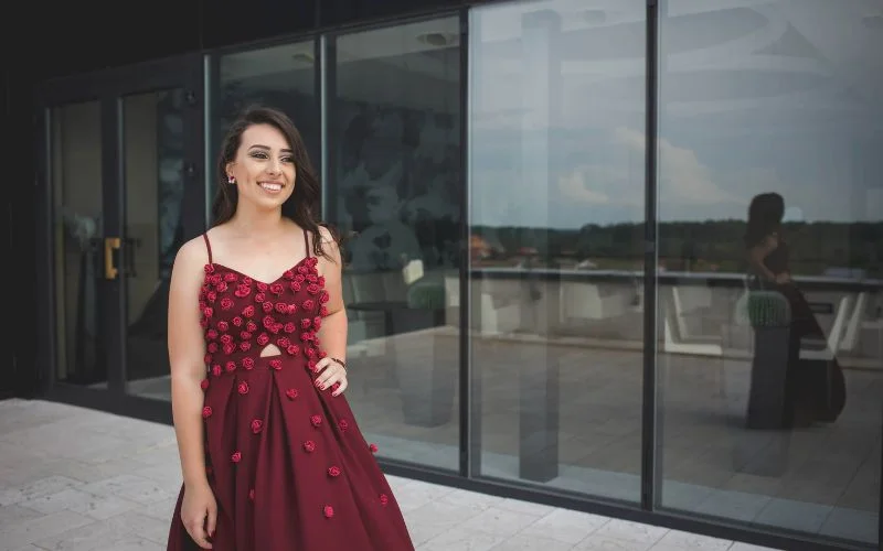 Prom pose for singles with a woman in a red gown standing solo by a window