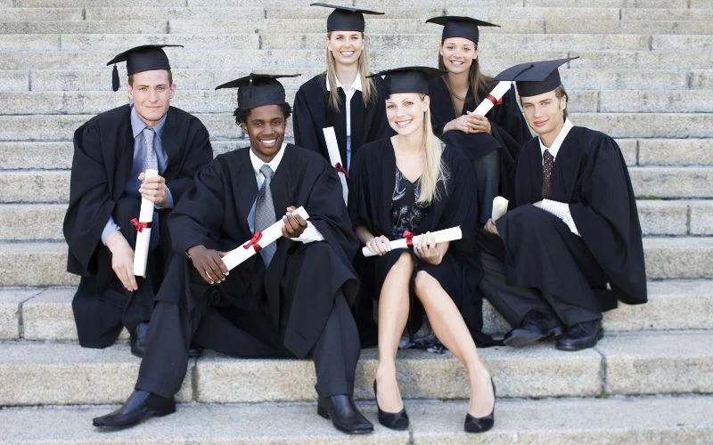 Grad picture poses of five graduates sitting together on outdoor stone steps holding diplomas