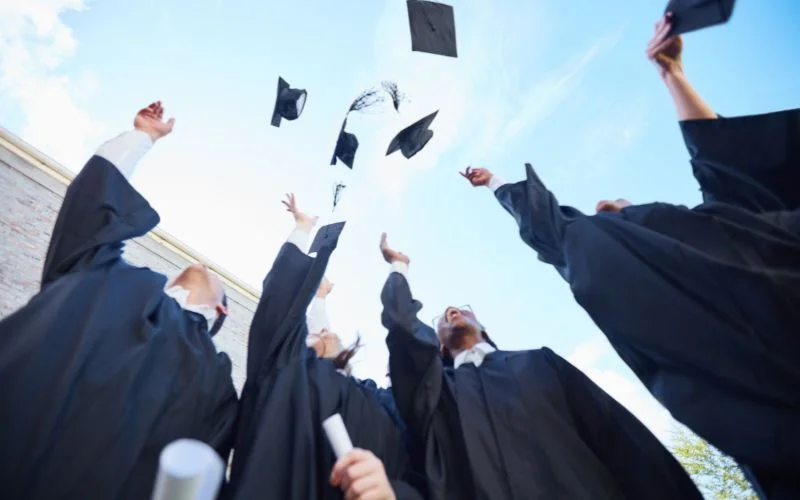 Group of graduates in caps and gowns throwing their caps into the air against a blue sky