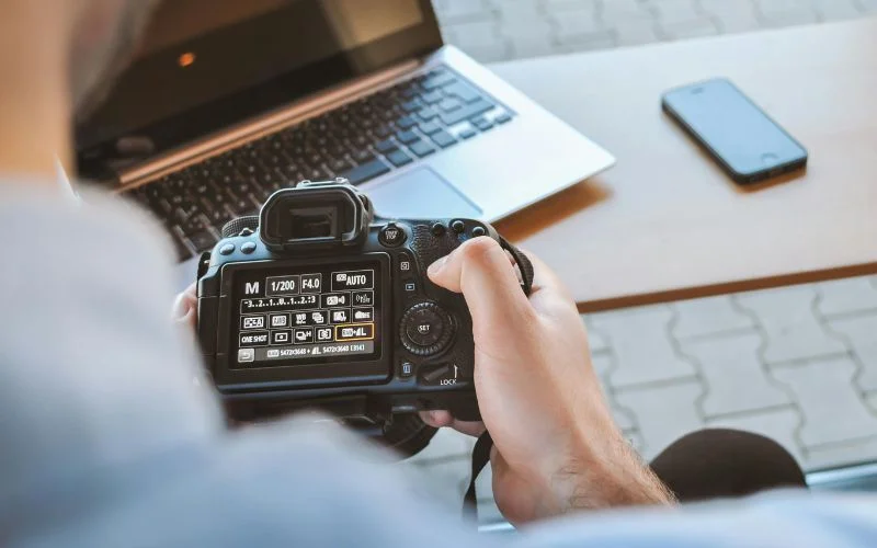 Photographer adjusting the shutter speed dial on a camera next to a laptop, showing what shutter speed is measured in