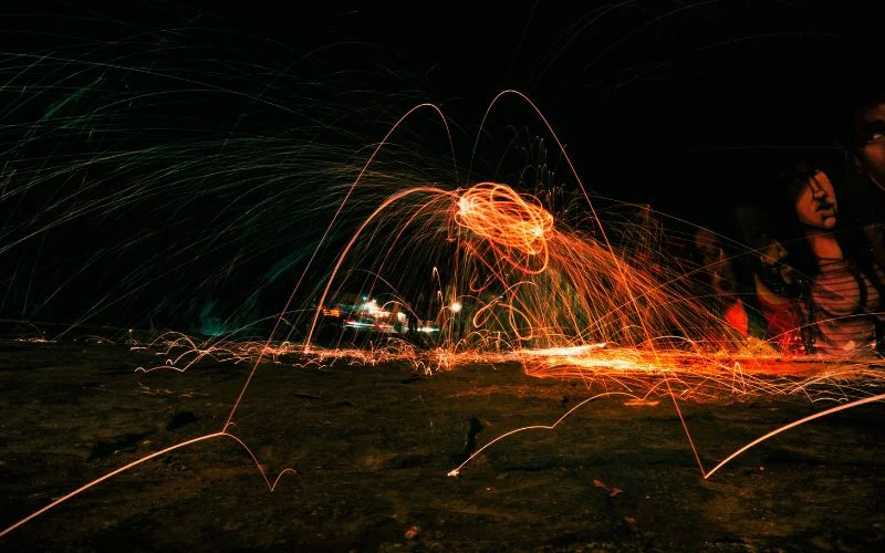 Glowing steel wool spun in circles at night creating bright orange light trail patterns