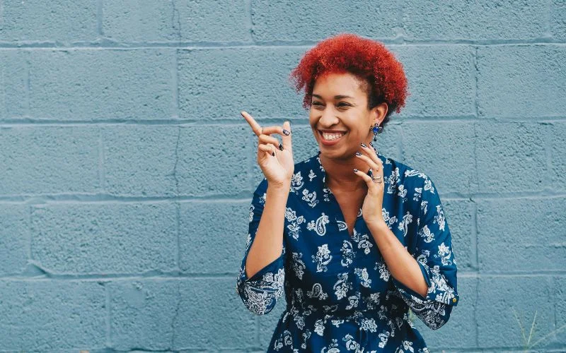 Woman with curly red hair smiling and pointing, a sharp handheld shot demonstrating camera shake prevention