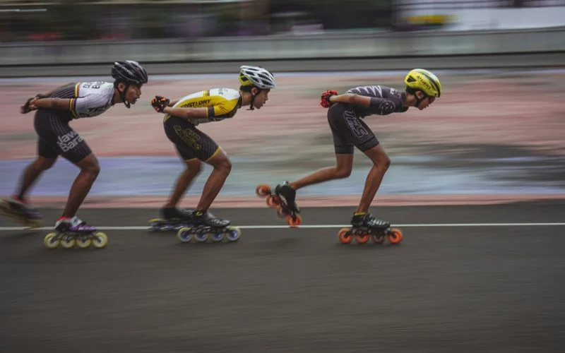 Three inline skaters racing with motion blur trailing behind them at dusk