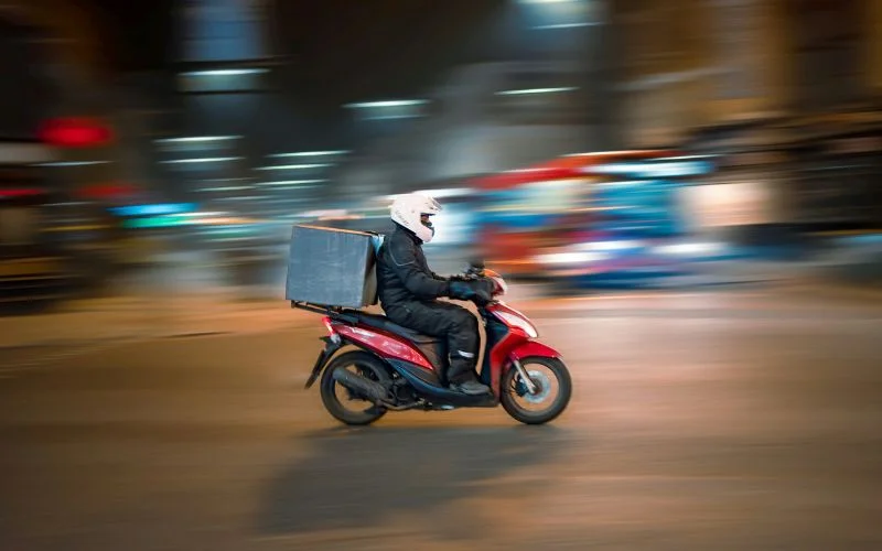 Delivery rider on a motorcycle captured with a panning shot, sharp subject against a blurred street background