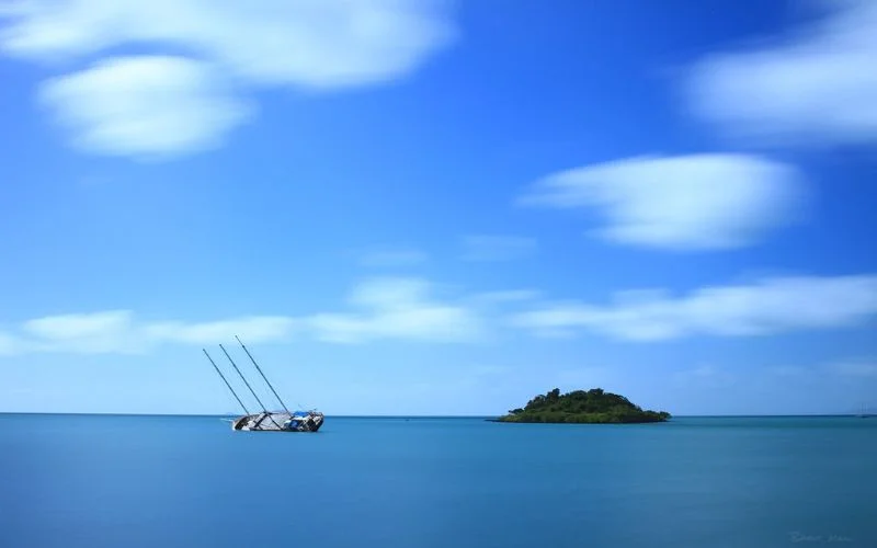 Calm ocean scene with a boat and island, clouds smoothed into streaks by a 30 second long exposure