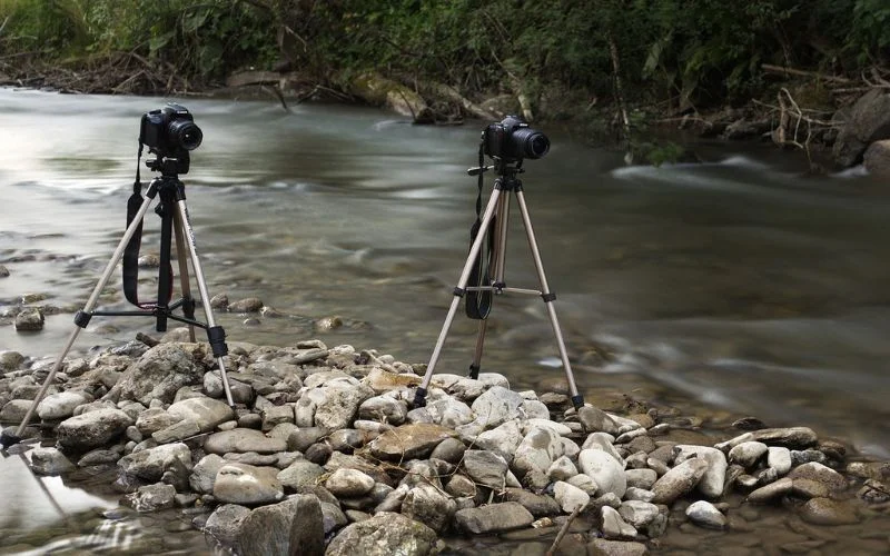 Camera tripod set up on rocks beside a flowing river for a stable long exposure shot