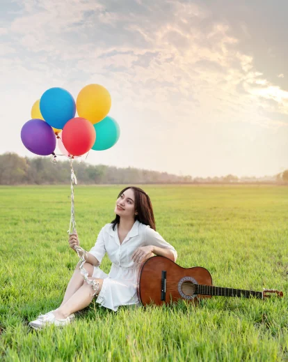 Woman sitting in a grass field with balloons and a guitar