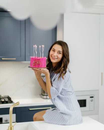 Woman in a kitchen holding a stack of cupcakes with lit candles