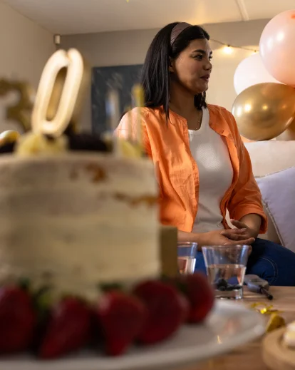 Woman in an orange cardigan at an indoor birthday party with balloons