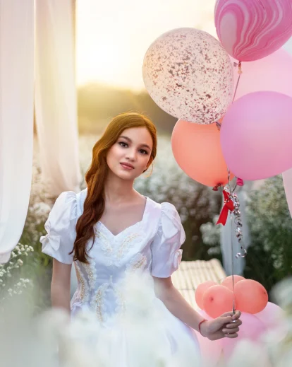 30th birthday photo idea of a woman in a white dress holding pastel balloons outdoors