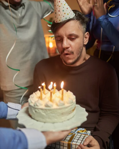 0th birthday photoshoot idea for him with a man blowing out candles on a cake surrounded by friends