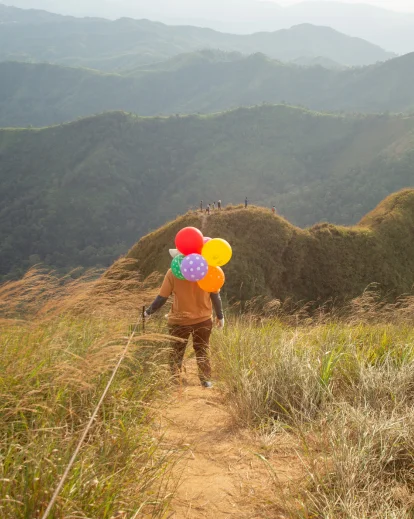 Unique 30th birthday photoshoot idea of a person walking a mountain trail holding colorful balloons