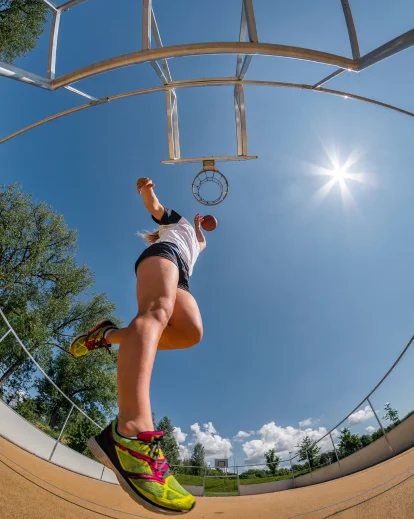 Woman performing a trick on outdoor gym bars against a bright sky
