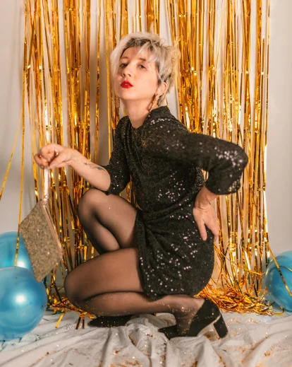 Woman in a flapper-style dress crouching against a gold fringe backdrop