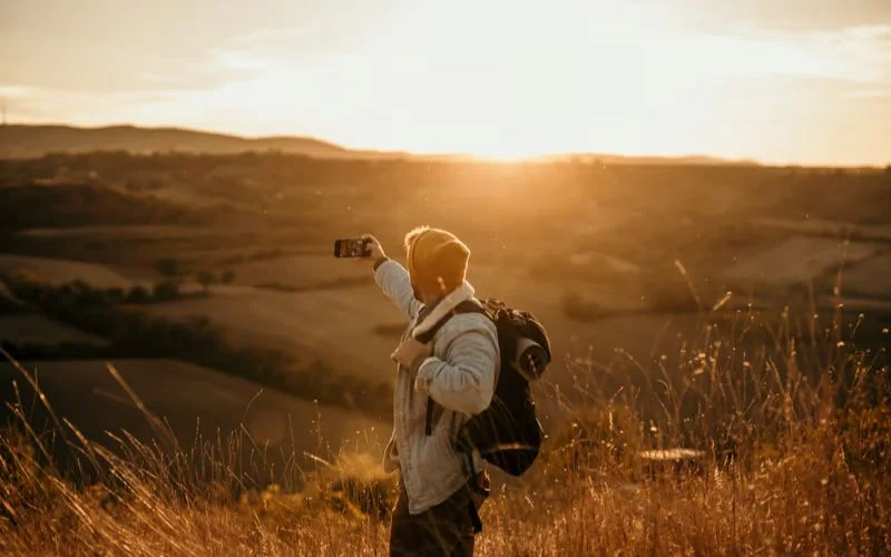 Photographer with a backpack using a tripod to photograph rolling hills during golden hour