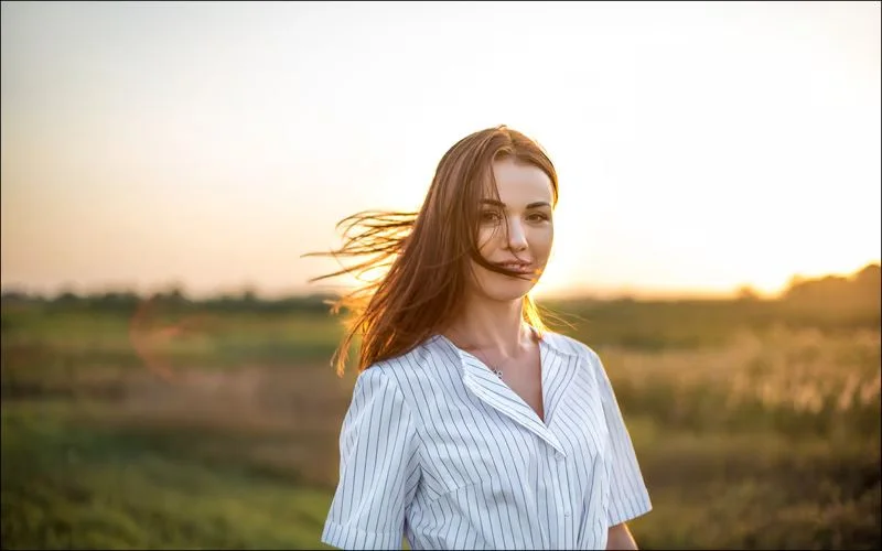 Woman with long hair blowing in the wind, backlit in a golden field during golden hour