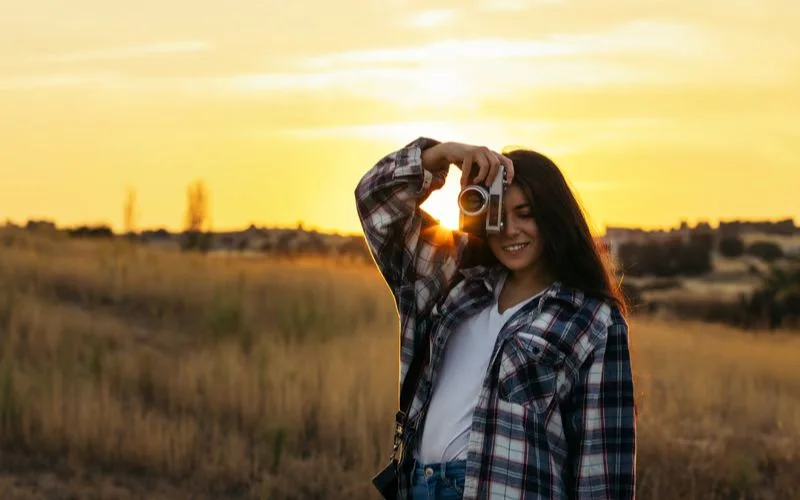 Woman in a plaid shirt forming a heart shape with her hands, backlit against the setting sun