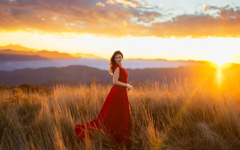 Woman in a red dress standing in a golden field at sunset, an example of best camera settings for golden hour portraits