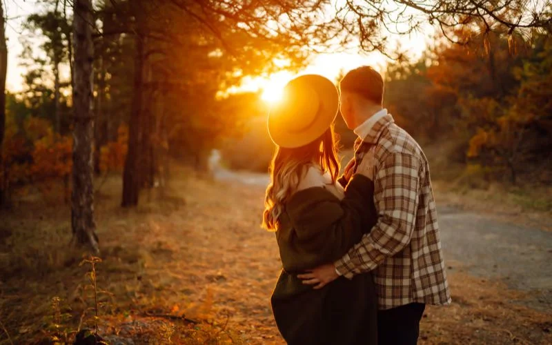 Couple embracing in an autumn forest, backlit with warm golden tones from golden hour photo settings
