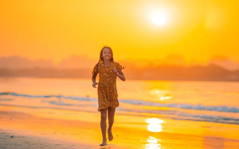 Silhouette of a girl walking along the shoreline at sunset with the sun low on the horizon